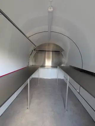 Vue d'ensemble des plans de travail inox sur pieds, de la porte vers le fond de la remorque